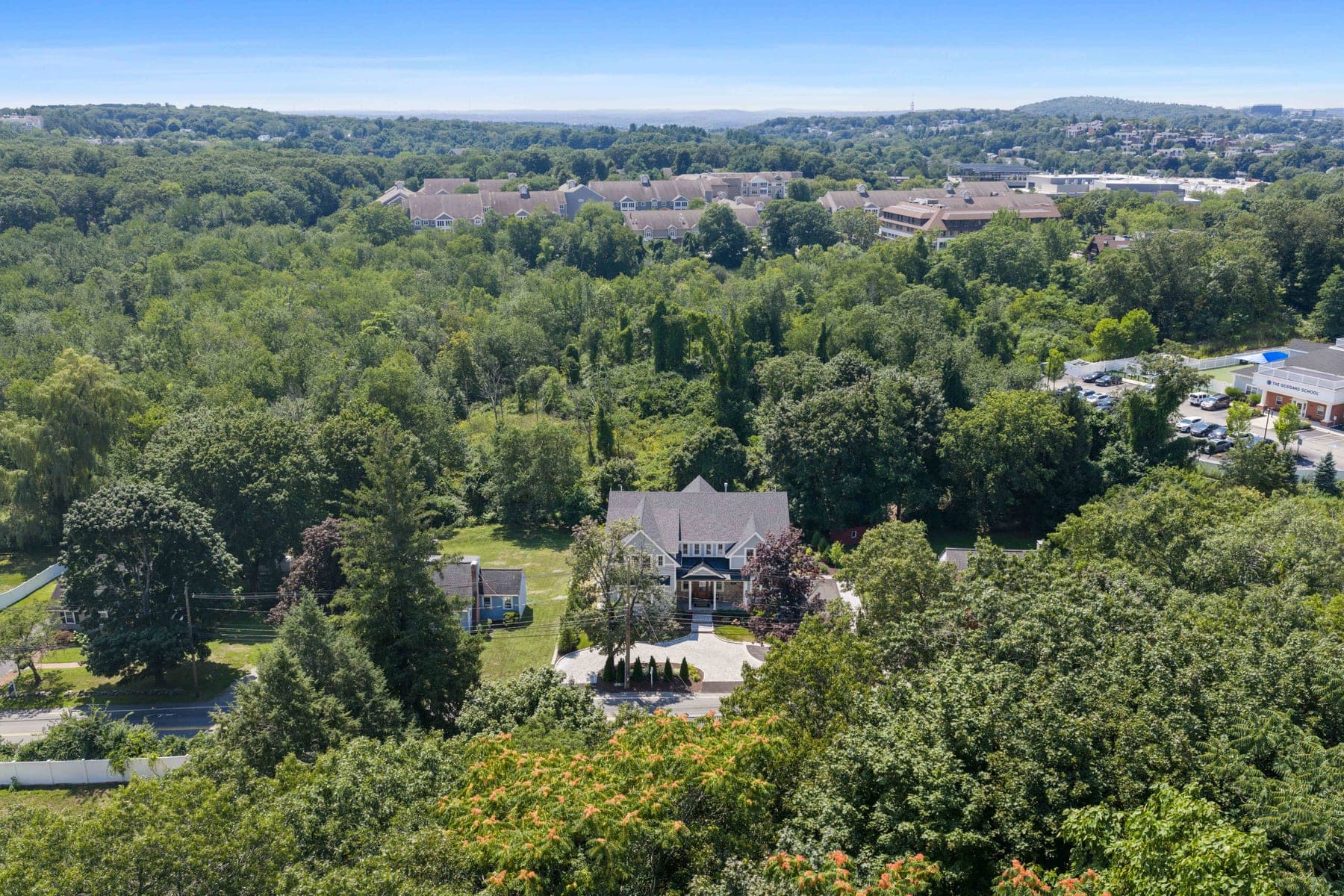 Wide aerial showing the home set among protected woodland with distant Lexington hills beyond