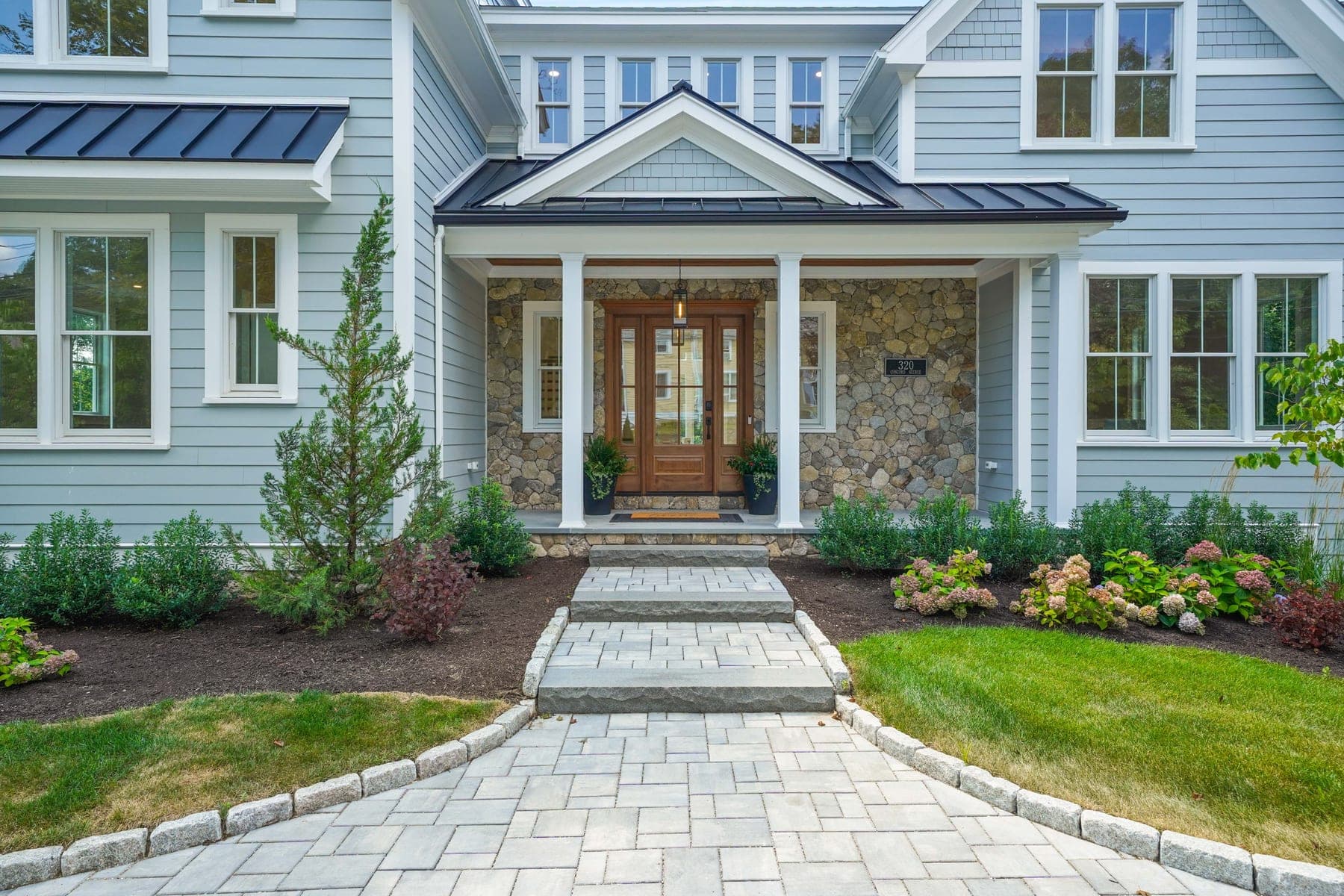 Front entry close-up with stone portico, mahogany door, address plaque, and blooming hydrangeas