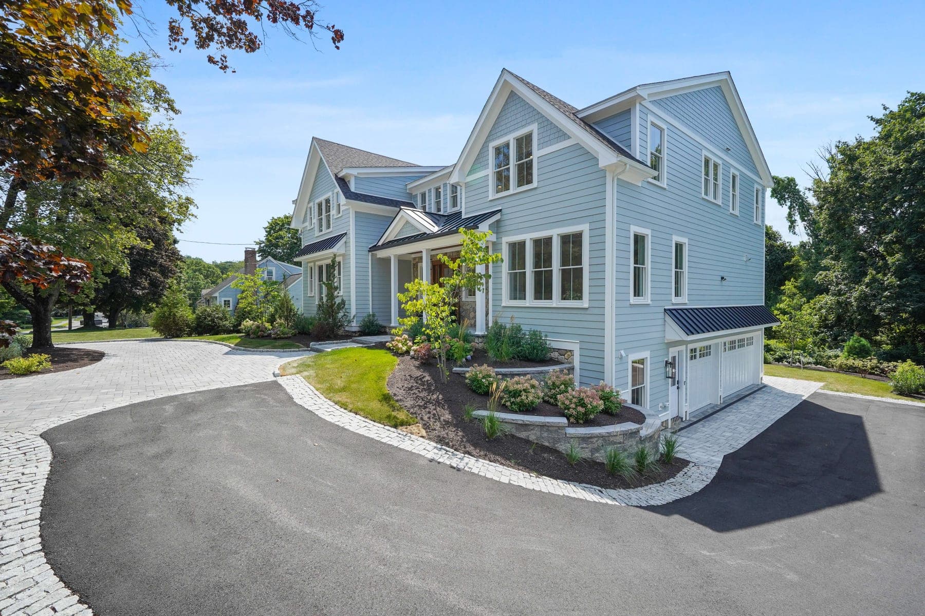 Front and side elevation showing the shingle-style architecture, garage, and mature summer landscaping
