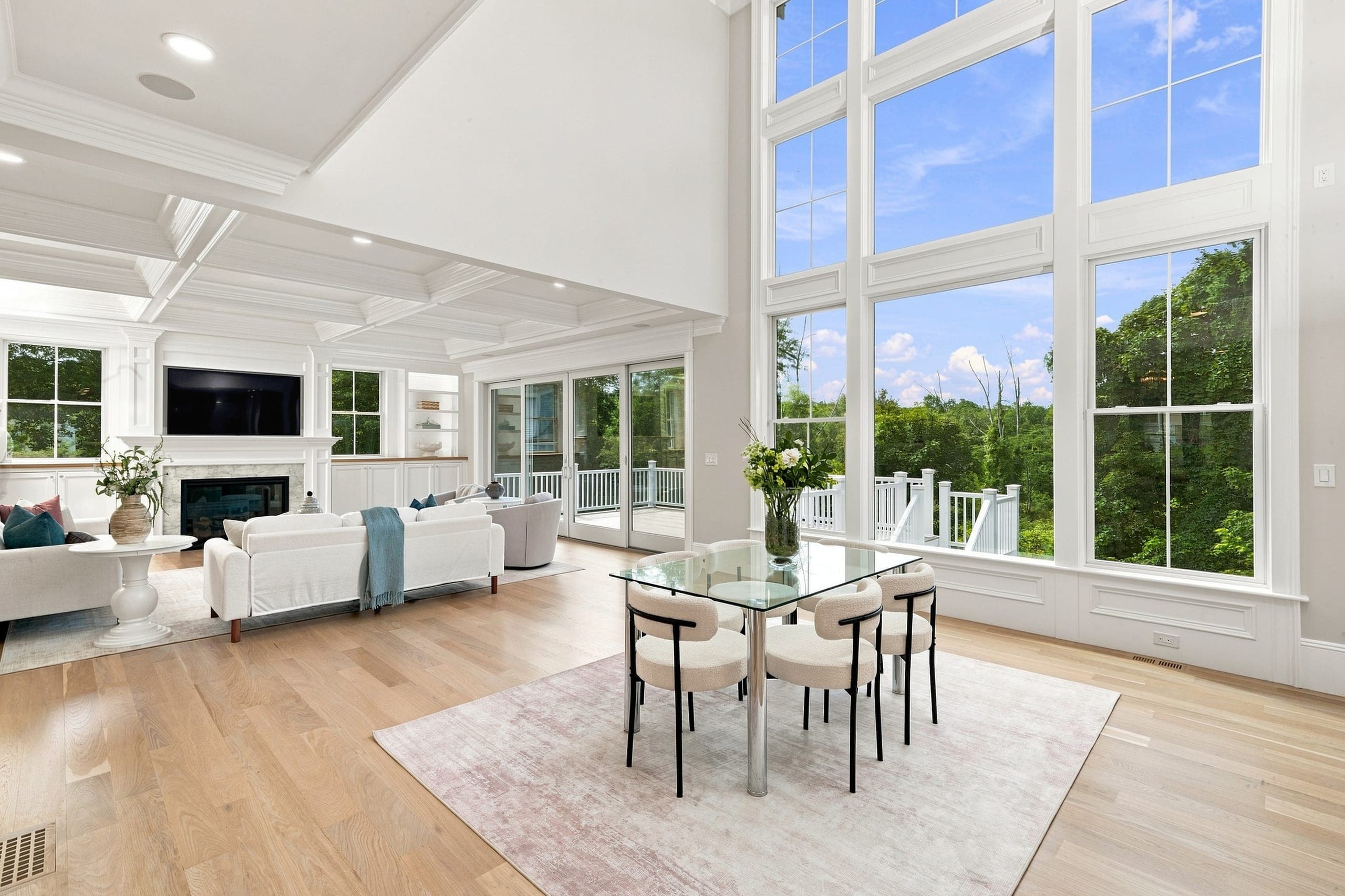 Family room framed by a wall of windows overlooking the private, wooded conservation land behind the home in full summer greenery