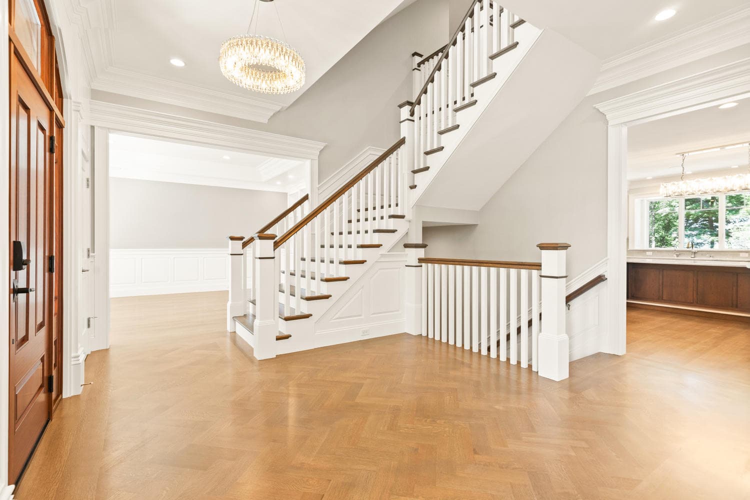 Grand foyer with herringbone oak floors, crystal chandelier, mahogany front door, and oak staircase