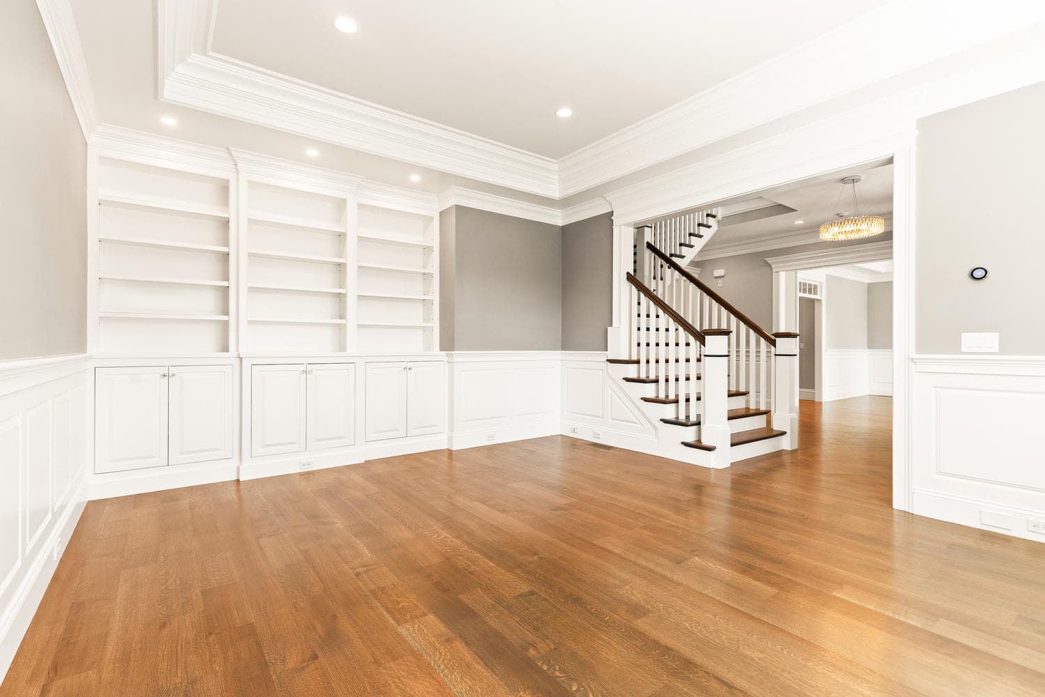 Living room with full-wall white built-in bookshelves, wainscoting, and staircase view