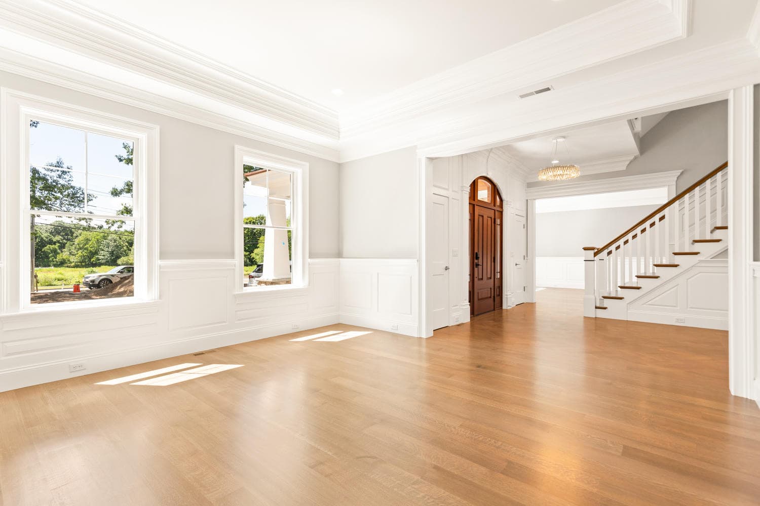 Expansive open living area with light oak floors, staircase, and French doors to deck