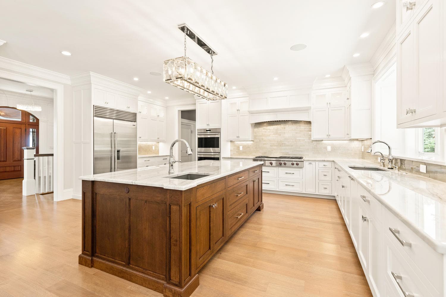 Chef's kitchen with white cabinetry, dark walnut island with marble countertop, Sub-Zero refrigerator, and crystal linear chandeliers