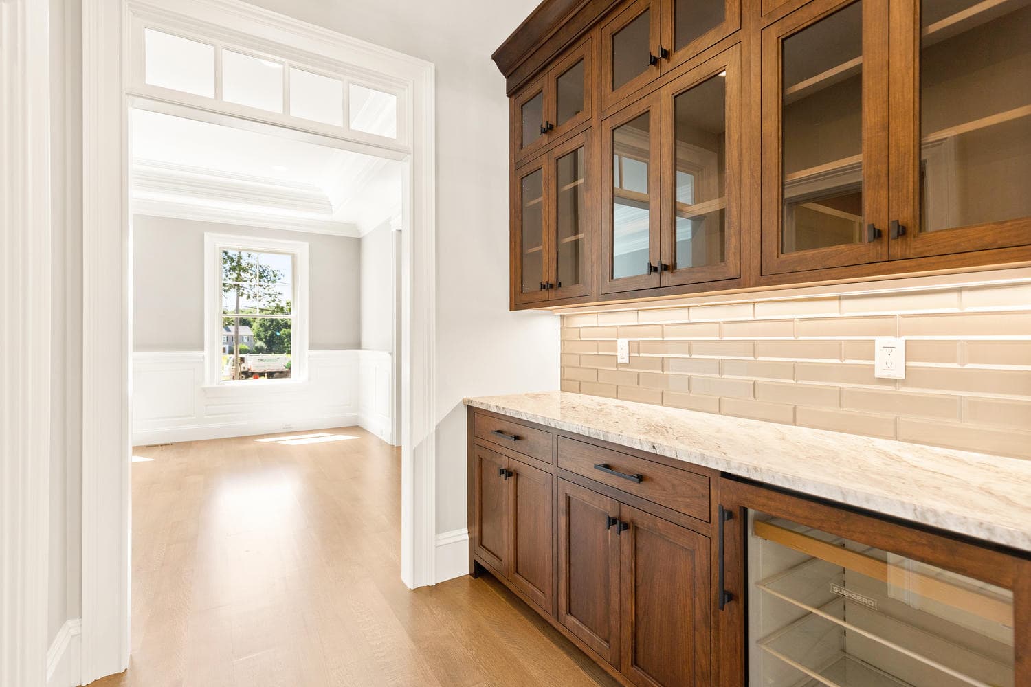 Butler's pantry with dark walnut glass-front cabinetry, subway tile backsplash, and Sub-Zero beverage refrigerator