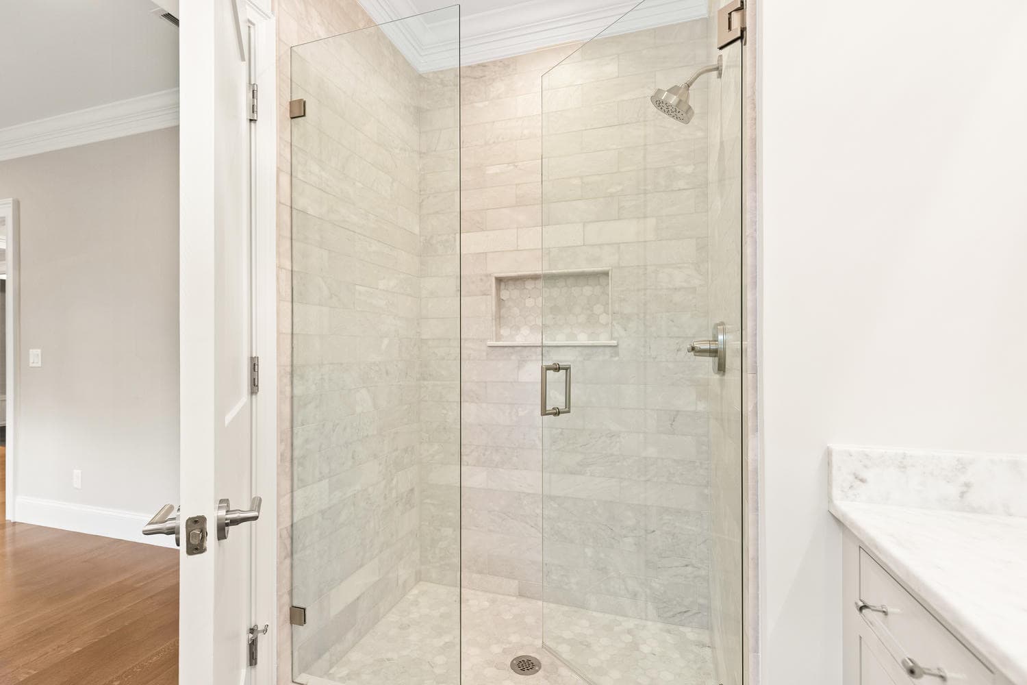 Primary bathroom with floor-to-ceiling marble tile shower, glass enclosure, and hexagonal mosaic niche