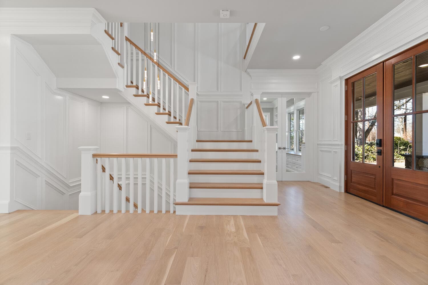 Grand foyer with two-story wainscoted walls, oak staircase, and mahogany French doors