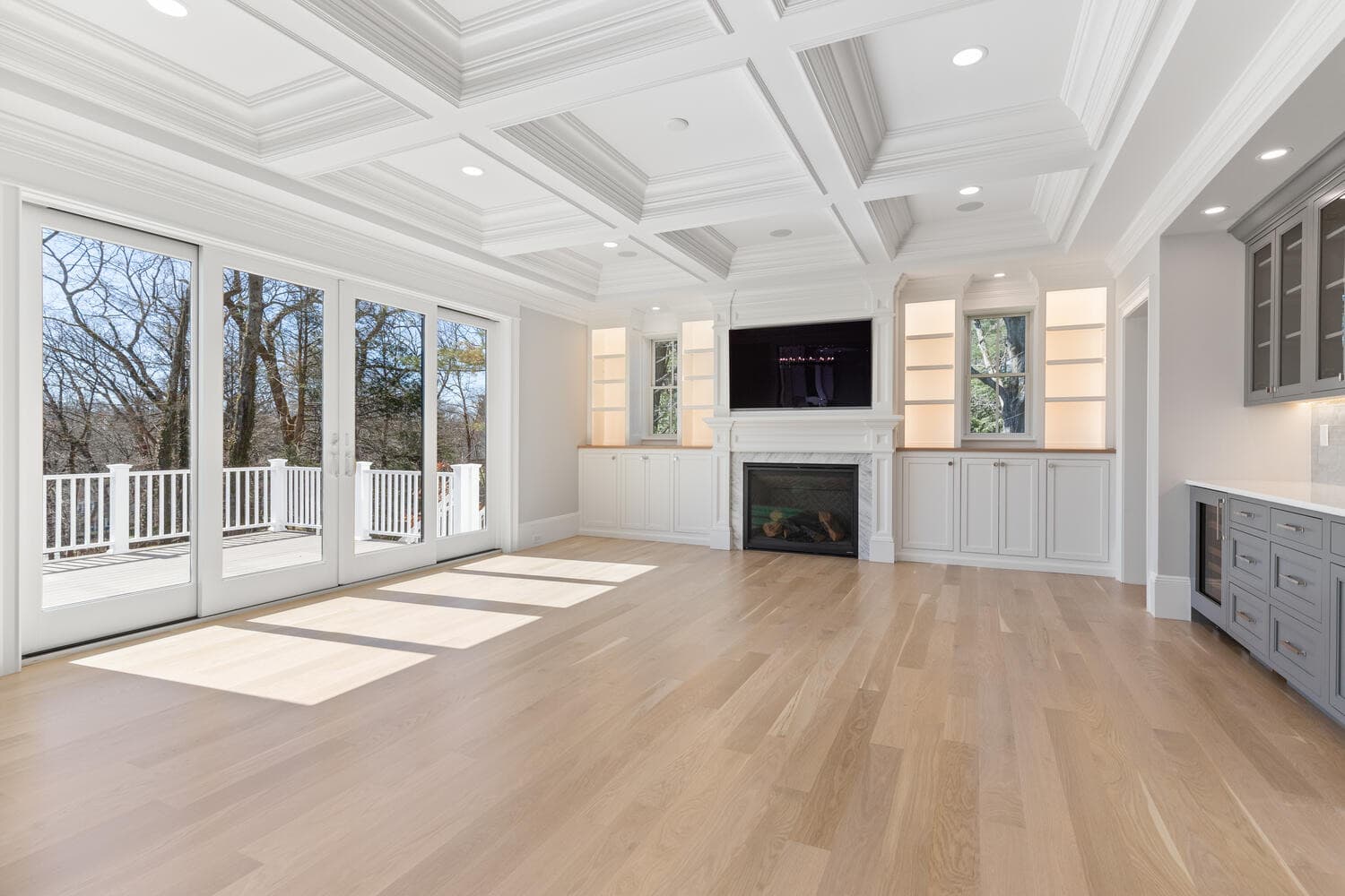 Great room with coffered ceiling, gas fireplace, built-in cabinetry, and sliding doors to deck