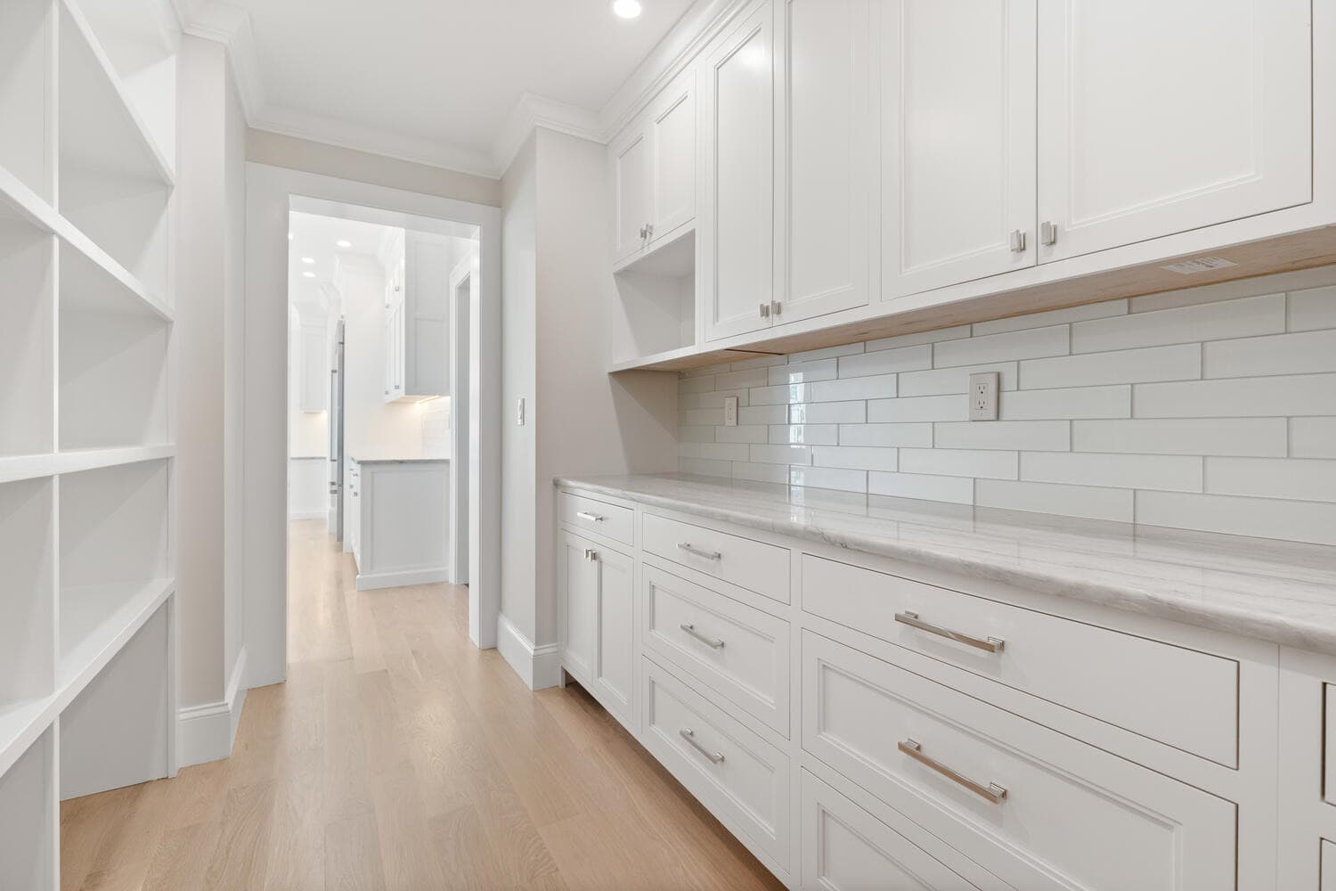 Walk-in pantry with white cabinetry, subway tile, and wine storage cubbies