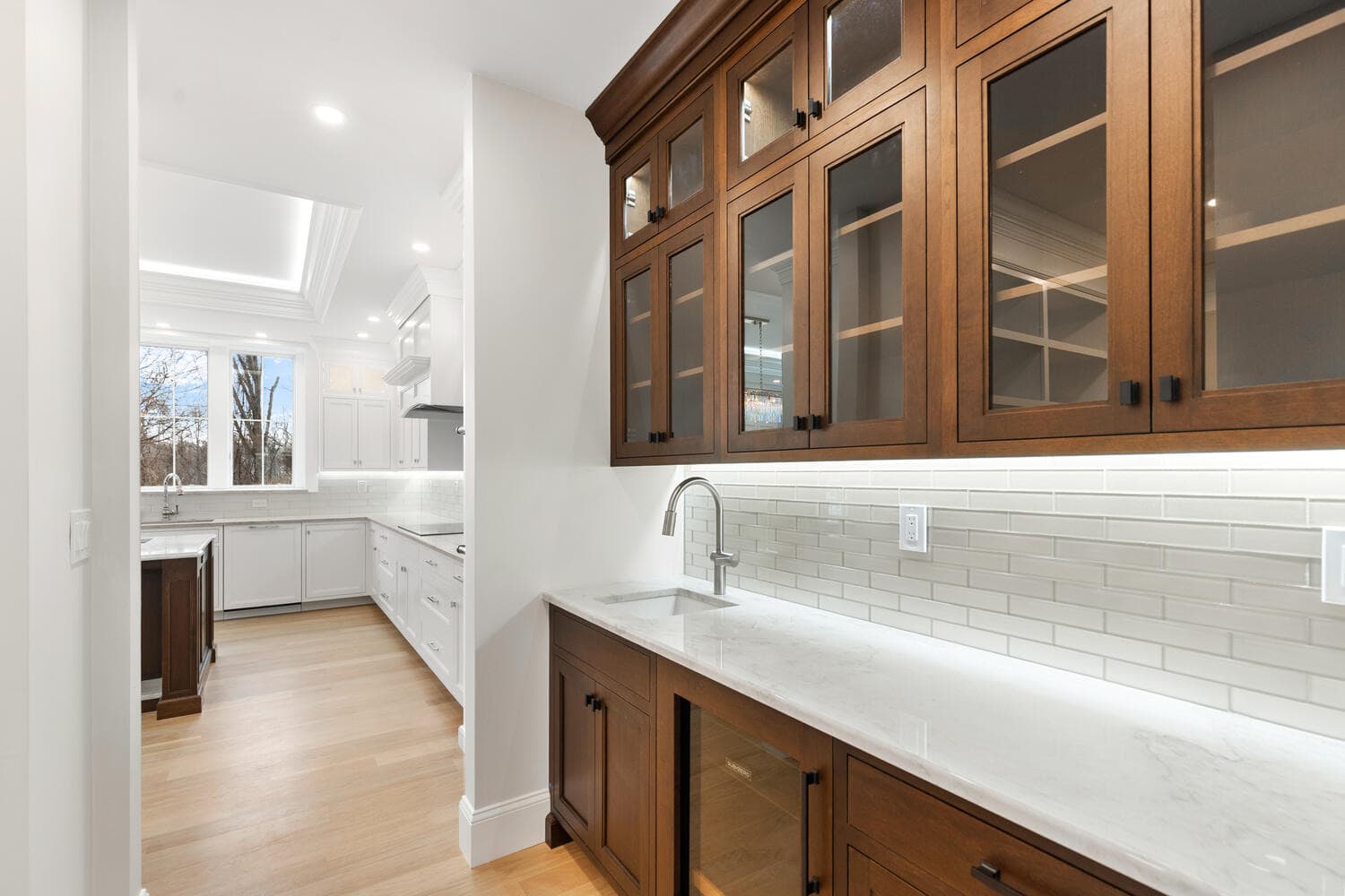 Butler's pantry with dark wood cabinetry, glass-front uppers, white marble counter, and subway tile