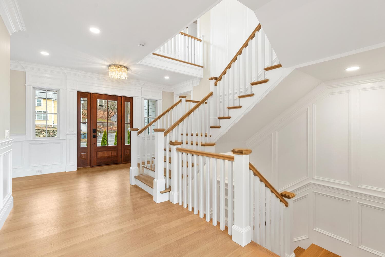 Grand foyer with two-story staircase, white spindles, oak treads, and entry doors