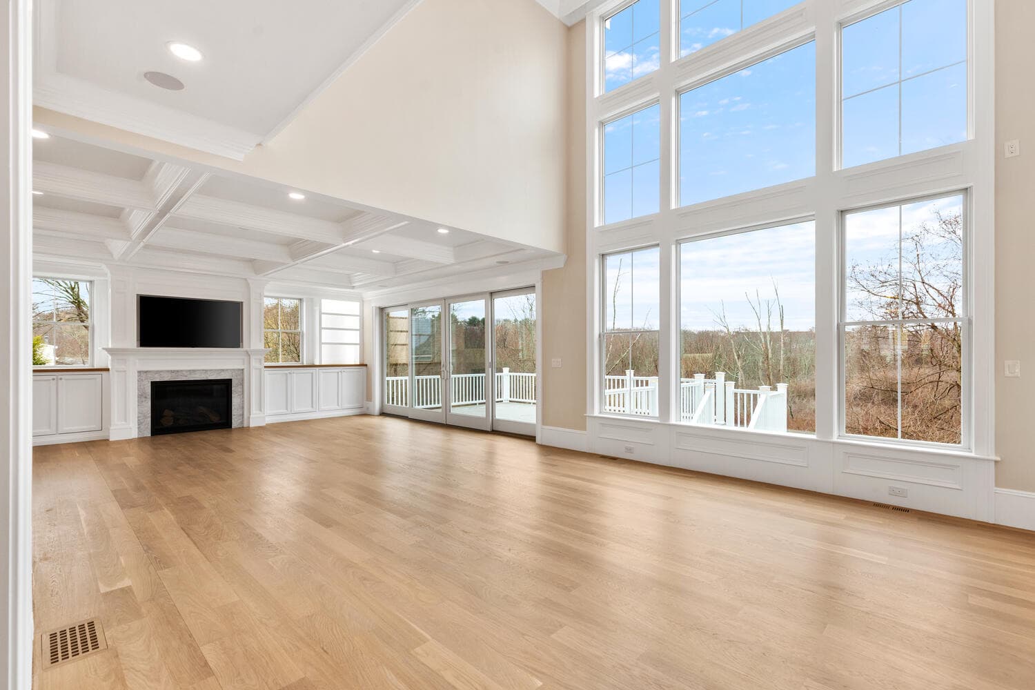 Great room with coffered ceiling, two-story Andersen window wall, fireplace with TV, and built-ins