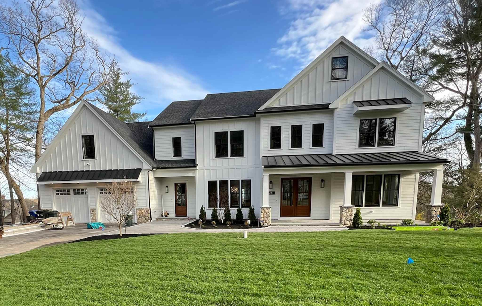 Modern farmhouse exterior with white siding, black metal roof accents, and mahogany entry doors